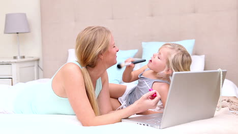 mother and daughter lying on bed using laptop