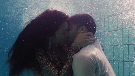 Pareja-Romántica-Besándose-Bajo-El-Agua-En-La-Piscina-Vistiendo-Ropa-Jóvenes-Enamorados-Disfrutando-De-Besos-íntimos-Amantes-Sumergidos-En-Agua-Flotando-Con-Burbujas-En-Intimidad-Apasionada