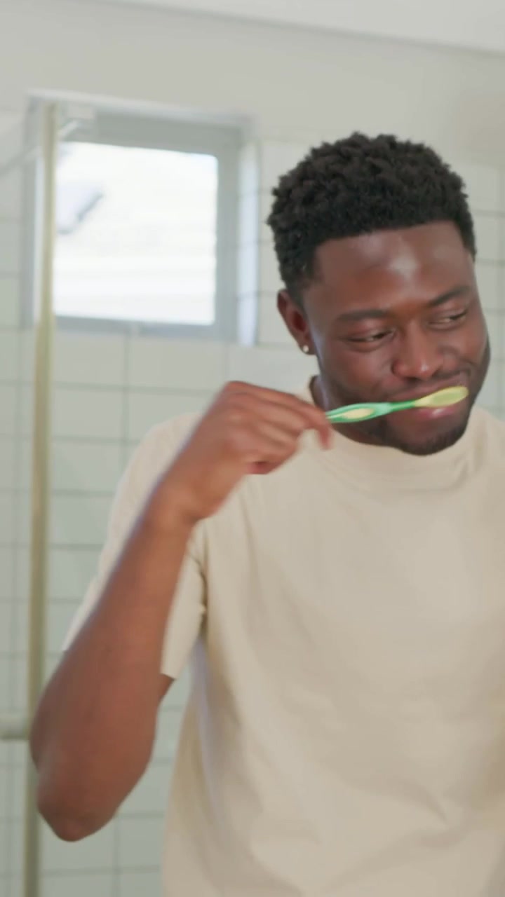 Vertical video: Grabbing green toothbrush, man brushing teeth at sink, beige tee, purple toothbrush
