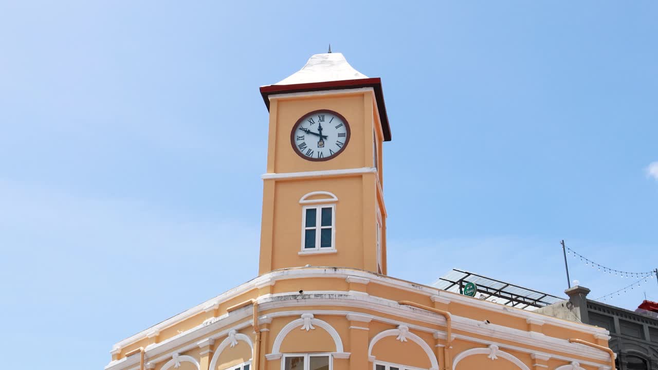 A clock tower stands tall in a sunny street scene as vehicles pass by, capturing urban life