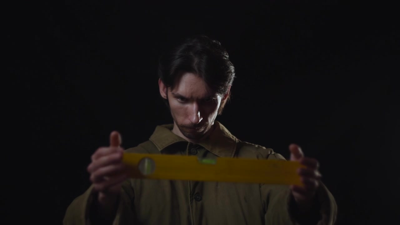 Um jovem com uma camisa escura está centralizado contra um fundo preto, olhando para baixo em um retrato silencioso e melancólico com forte sombra e contraste