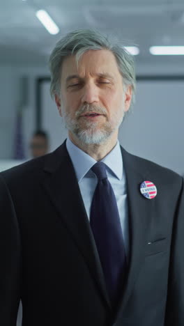 businessman with badge speaks on camera and calls for voting in modern polling station. portrait of man, united states of america elections voter. background with voting booths. concept of civic duty.