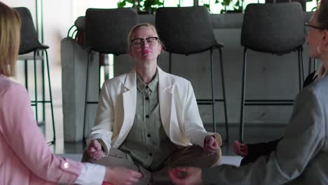 a group of confident businesswomen in business clothes meditate while sitting on the carpet during their break between work in a modern office