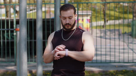 athletic lebanese man in sportswear using smart watch listening music on earphones on playground