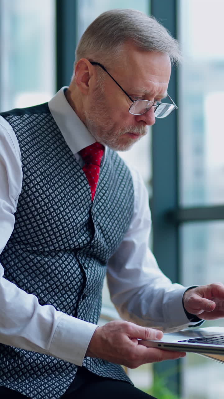 Thoughtful businessman working on computer in front of the window with city view. Video of working process in big company. Vertical video
