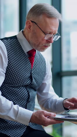 thoughtful businessman working on computer in front of the window with city view. video of working process in big company. vertical video