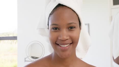 Portrait-of-happy-biracial-woman-with-towel-on-head-in-bathroom,-slow-motion