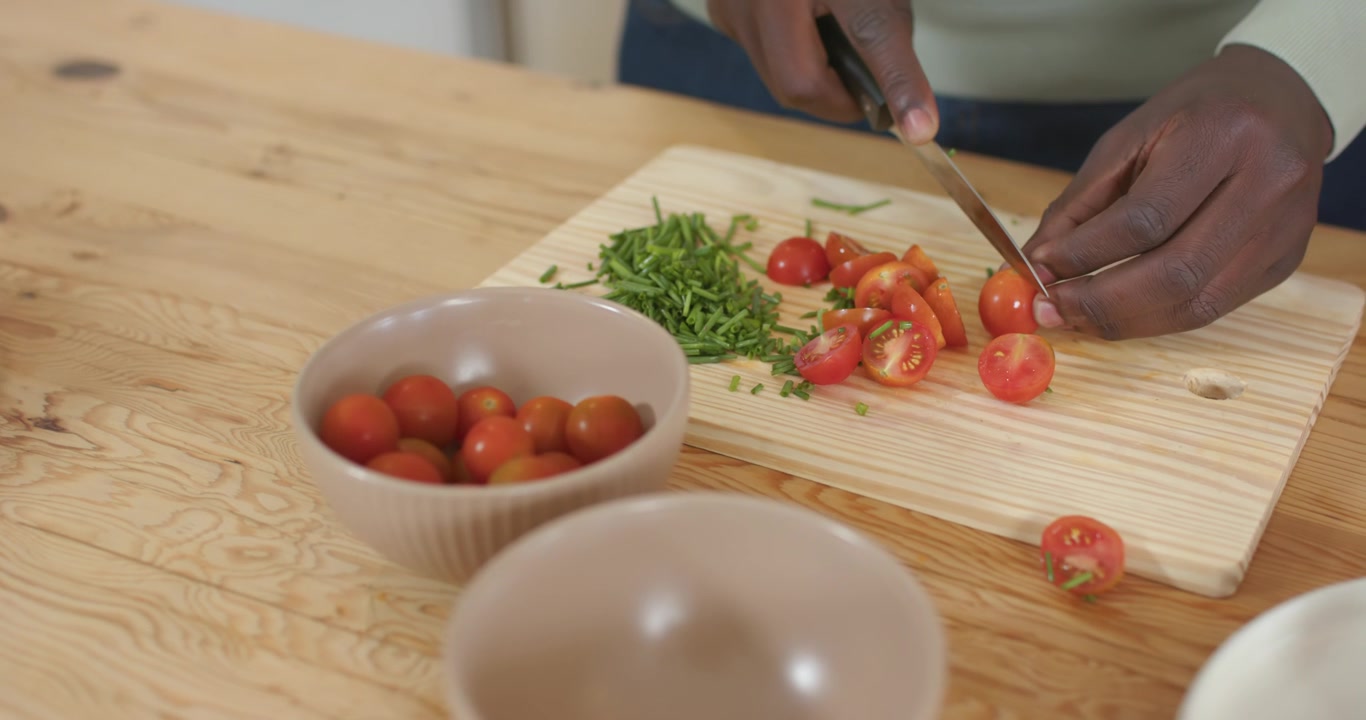 Donna afroamericana che posiziona un pomodorino sul tagliere, affettando con un coltello per la preparazione dell'insalata.