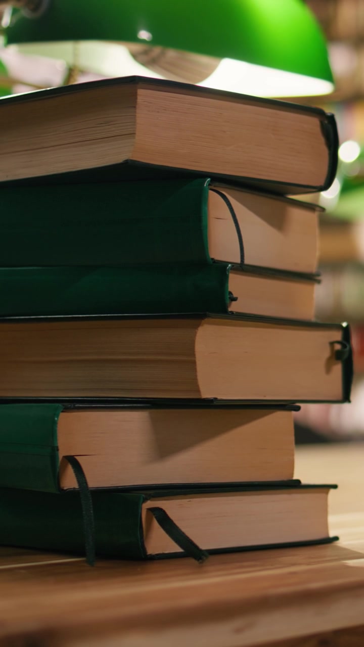 Vertical Video Stack of books on desk in quiet university library with warm lighting