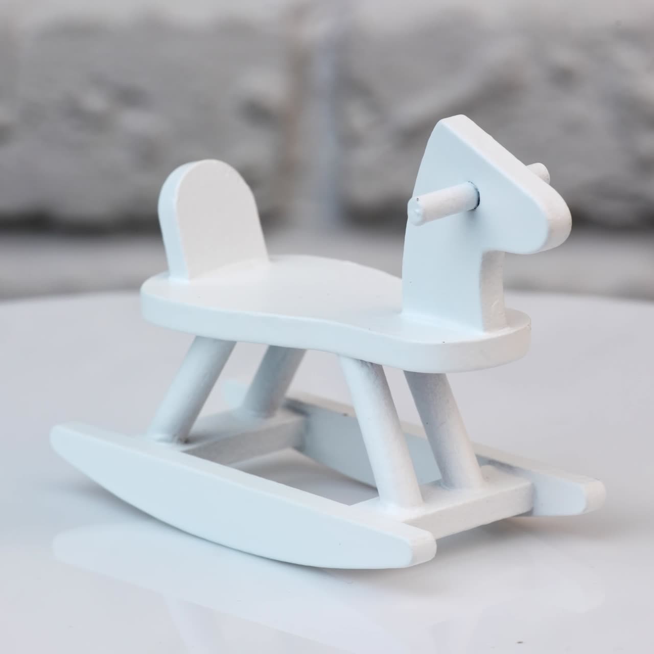 Small wooden rocking horse on a rotating table. Toy rocking horse for a doll's house. Tiny toy painted white. Close up