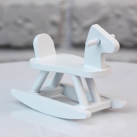 small wooden rocking horse on a rotating table. toy rocking horse for a doll's house. tiny toy painted white. close up