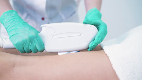 woman in green gloves does laser epilation of client legs