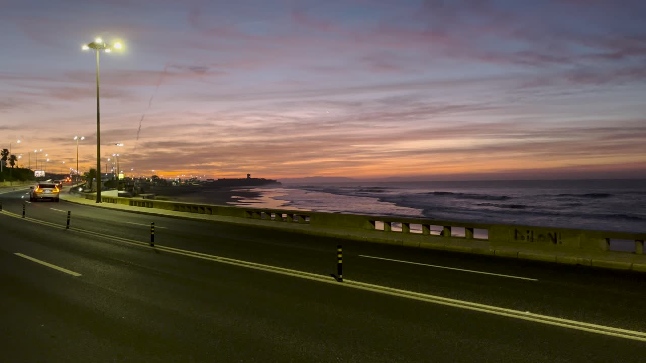 Static view of a road with cars passing by the sea. Night