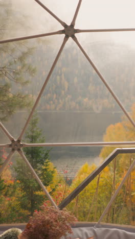 glamping terrace with view of lake and mountains in autumn. premise of country house with panoramic windows overlooking dense forest in cloudy weather