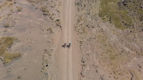 aerial shot following two mountain bikers climbing up a gravel road mountain pass