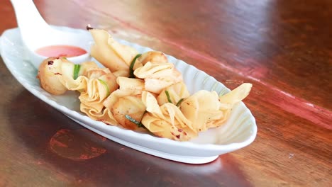 a hand arranges thai dumplings on a plate with sauce, showcasing a close-up view on a wooden table.