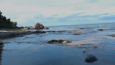 footage of ocean sea water waves moving in slow motion during the summer time while the sun is shining through cloudy and blue sky with a sandy shoreline visible with rock and vegetation in 4k quality