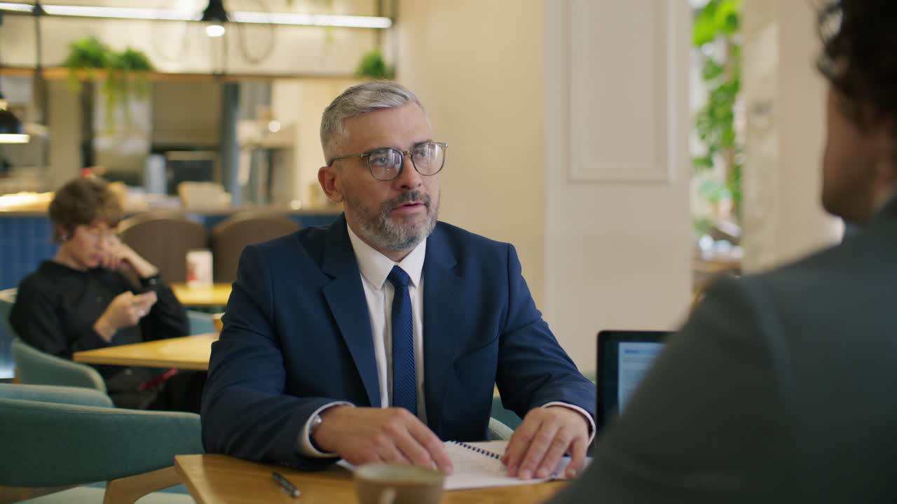 Senior leder forklarer rapport til forretningspartner ved møde på café