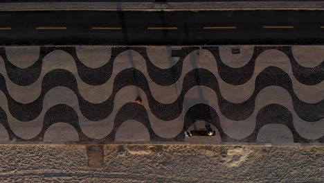 sideways aerial panning showing the patterns in the sidewalk pavement, bicycle lane and beach of copacabana at sunrise