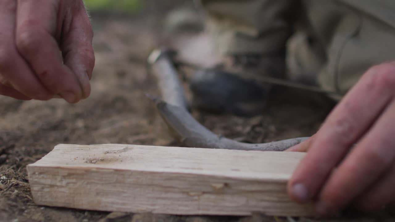las manos de un sobreviviente caucásico añadiendo tierra seca para preparar una tabla de fuego en un campamento en el desierto