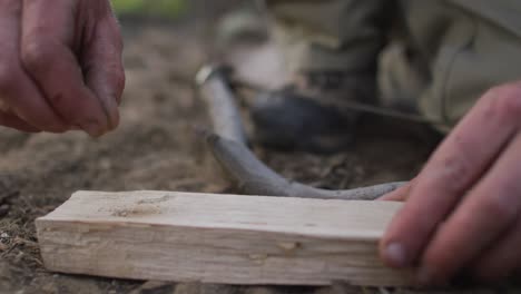 hands of caucasian male survivalist adding dry earth to prepare fireboard at camp in wilderness