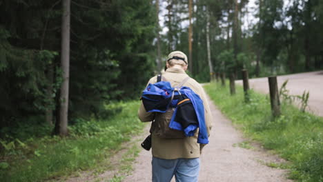 young man with backpack and camera walks on gravel path by forest