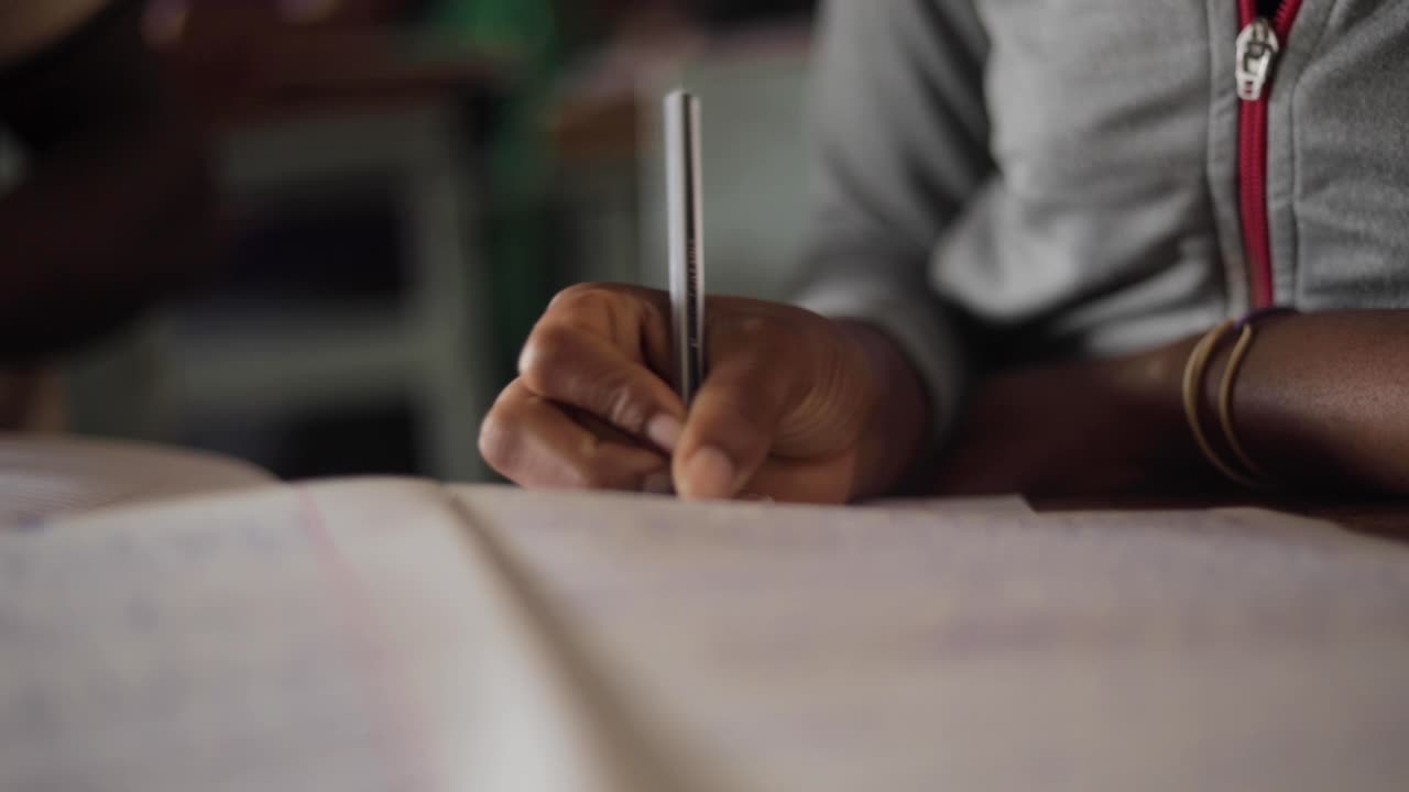 Close up shot African young kids children school students is writing with pencil doing homework in education class behind desk in village learning for the future job Tanzania 25 fps slowmotion