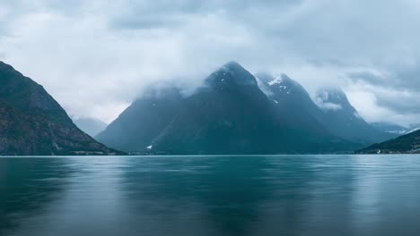 timelapse taken during the evening, on the surface of the water, looking over a beautiful lake with snow covered mountains in the background, clouds passing by, norway