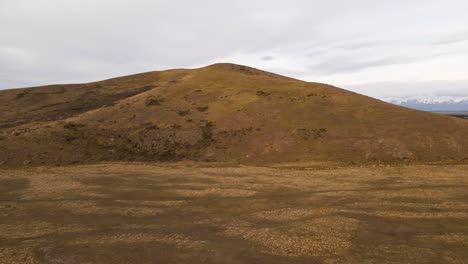 Fast,-wide-angle-aerial-footage-flying-over-a-brown-hill-to-reveal-a-snow-capped-mountain-range-of-the-New-Zealand-Alps