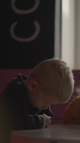 upset little boy and girl left without dessert lean on empty round table sitting in restaurant against blurry window and word covid-19 on board closeup