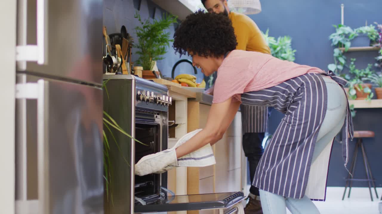 Vídeo de casal feliz e diverso de aventais assando juntos na cozinha, usando o forno, com espaço para texto