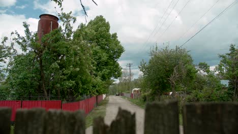 Macadam-stone-path-in-rural-village-surrounded-by-wooden-fences,-establishing-shot