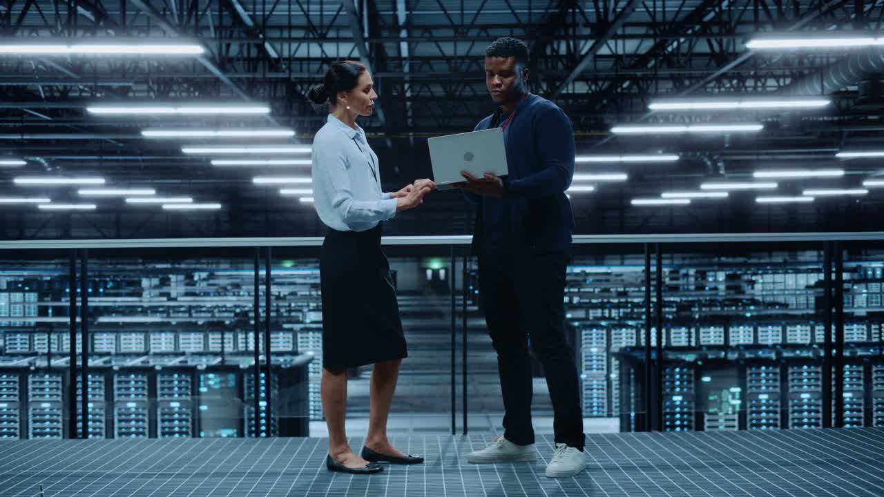 Amministratrice di sistema donna e Specialista IT uomo in un Data Center parlano e usano un computer portatile. Ingegneri dell'Information Technology lavorano sulla protezione della rete di sicurezza informatica in una Server Farm di Cloud Computing