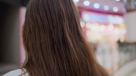 primer plano del cabello de una joven mientras sale de una escalera mecánica en movimiento en un vibrante centro comercial, capturando la atmósfera dinámica y su movimiento