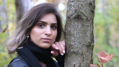 primer plano de una chica morena en el bosque de otoño se encuentra junto a un árbol y sonríe a la cámara - sacude el pelo corto