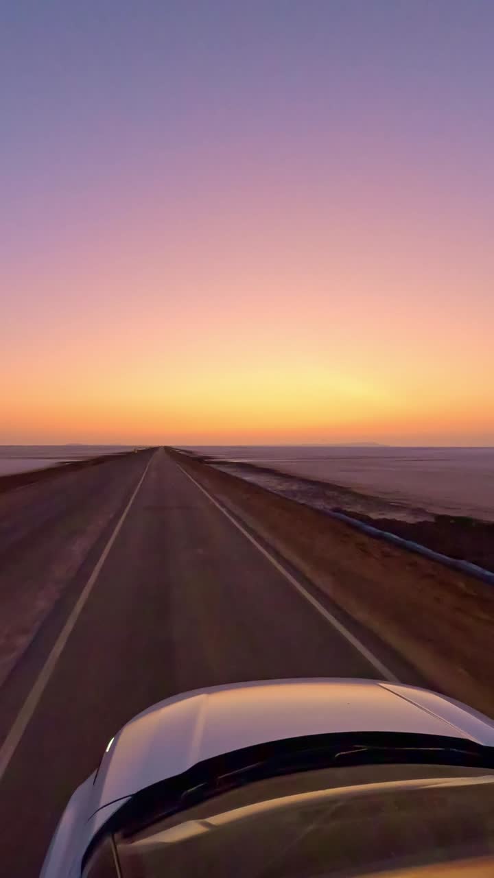 Driving forward on the road to heaven in Kutch, Gujarat, India the glowing white Rann shimmers endlessly on both sides while the sunset paints the sky in vibrant hues of orange and pink 4K