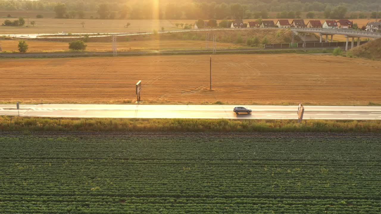 해가 지는 아름다운 시골을 가로질러 움직이는 은색 자동차 - 공중 드론 촬영