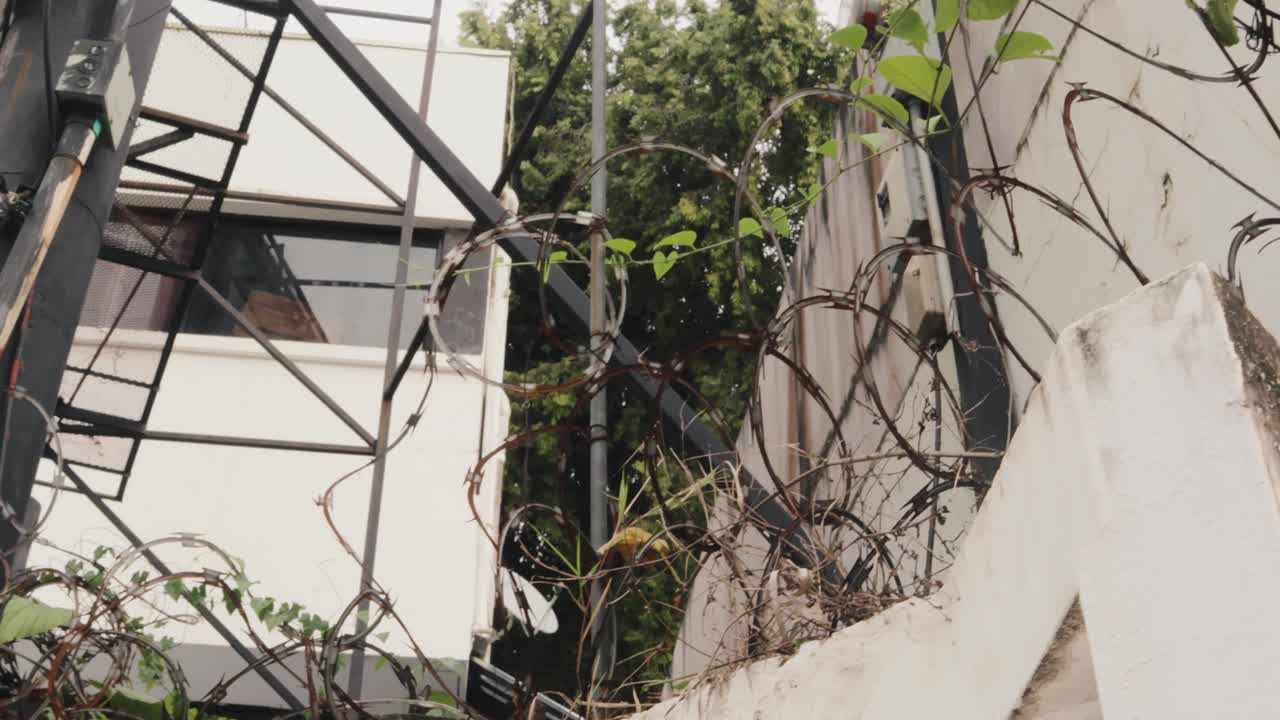 toma panorámica de derecha a izquierda de una cerca de alambre de metal con una casa blanca detrás rodeada de vegetación verde en la ciudad
