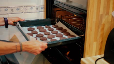 close up of female arms putting cookies in the oven