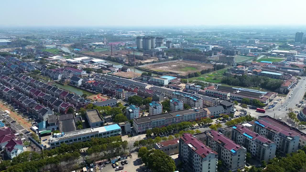 Aerial footage of Taicang in Jiangsu Province, China, captures residential housing, mid-rise buildings, roads, and semi-rural surroundings under clear skies.