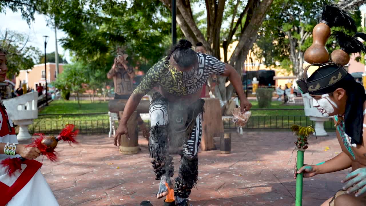 Slow motion Mayan and Aztec dancers performing, grabbing fire and blowing into a conch shell in a park outside in Valladolid, Yucatan, Mexico