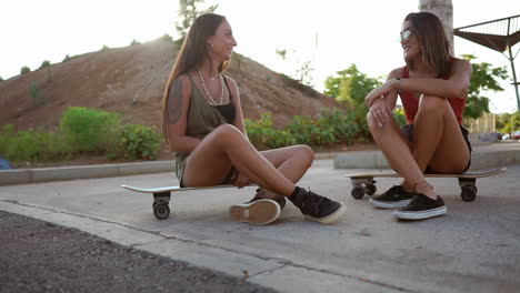 as the sun sets, two girls share a cheerful scene at the skate park, seated on their boards, chatting, laughing, and reveling in the relaxed atmosphere. longboard camaraderie