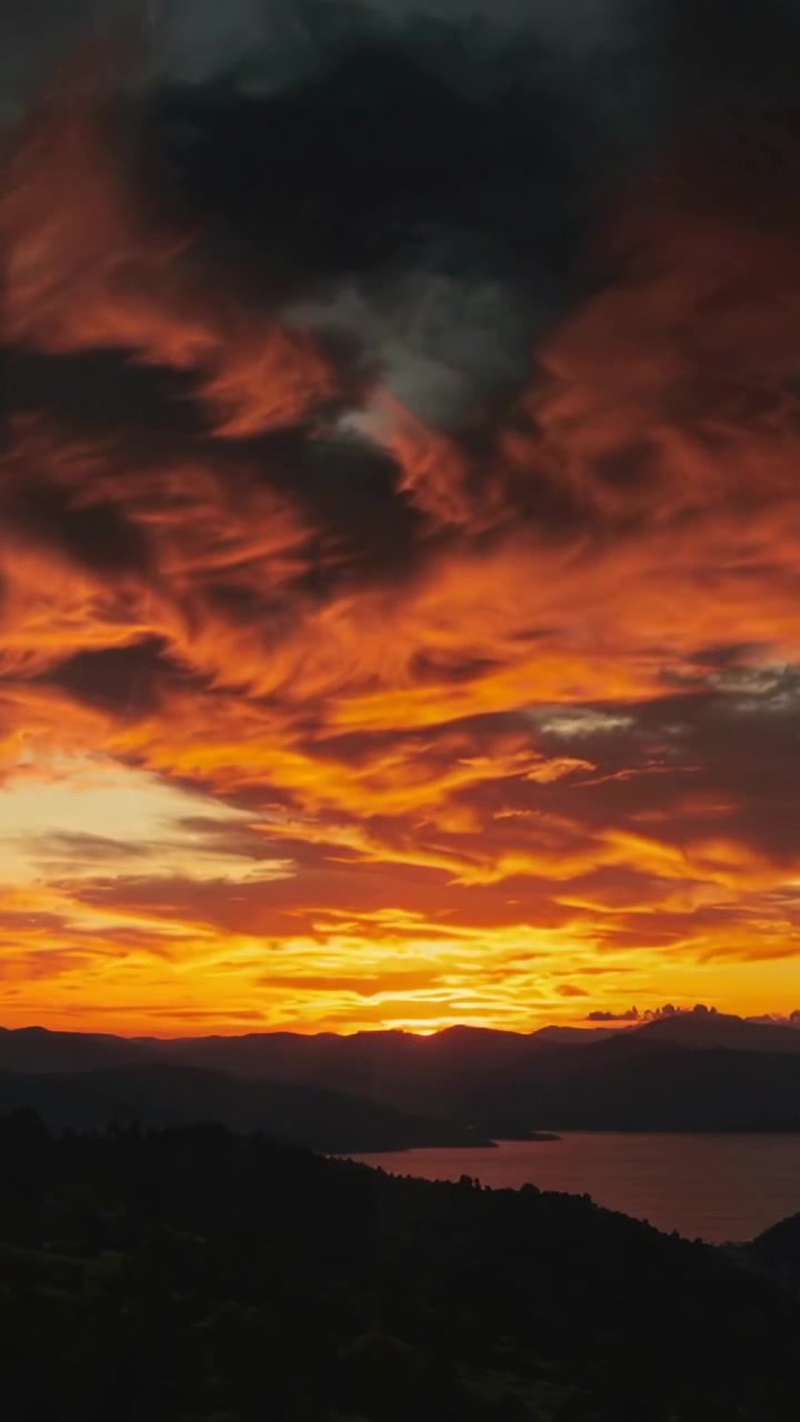Vertikales Video: Sich auflösende Frau im Mantel verschmilzt mit Sonnenuntergangsküste, Himmel-Overlay regt zum Nachdenken an.