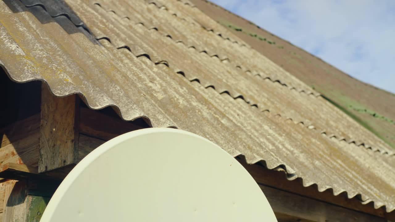 A close-up of a satellite dish fixed to a weathered corrugated metal roof on a rustic wooden structure. Daugavpils, Latvia (Latgale)