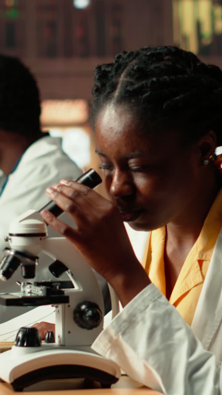 Scienziata afroamericana sorridente che alza lo sguardo dal microscopio