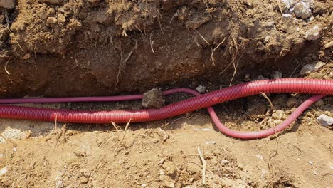 close up: red plastic telecommunication conduits run along a shallow trench.