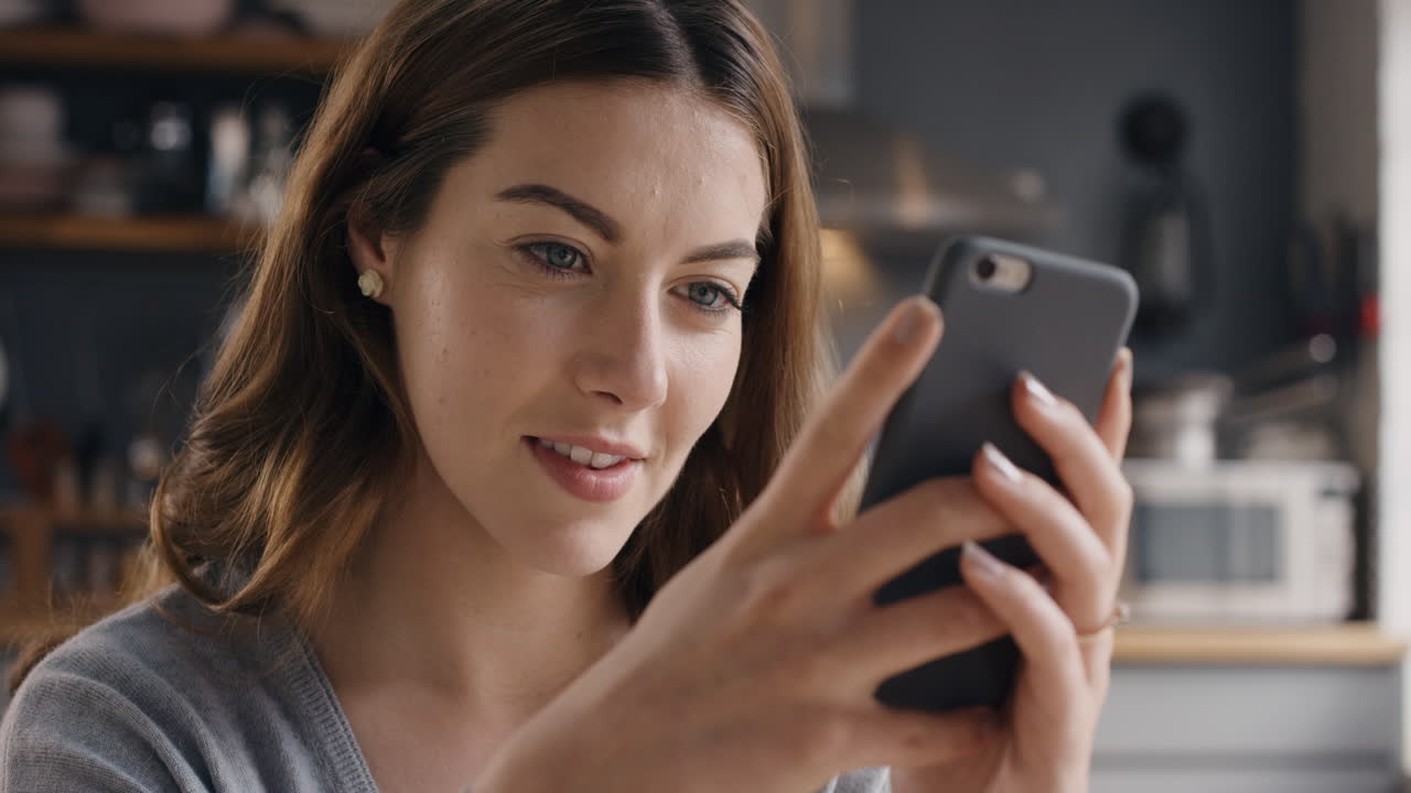 Attraktive Frau zu Hause benutzt in der Küche ihr Smartphone und sendet Nachrichten in sozialen Medien.
