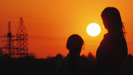 mom and daughter are watching the sunset over the urban horizon