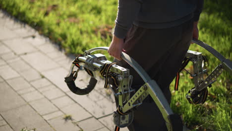 guy holding spring-loaded metal stilts with orange straps, wearing dark pants, standing on paved surface with grassy background, emphasizing innovative equipment and outdoor setting with dynamic