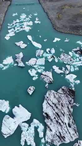 aerial drone footage view looking down on the jökulsárlón lake of icebergs in iceland, vertical video.